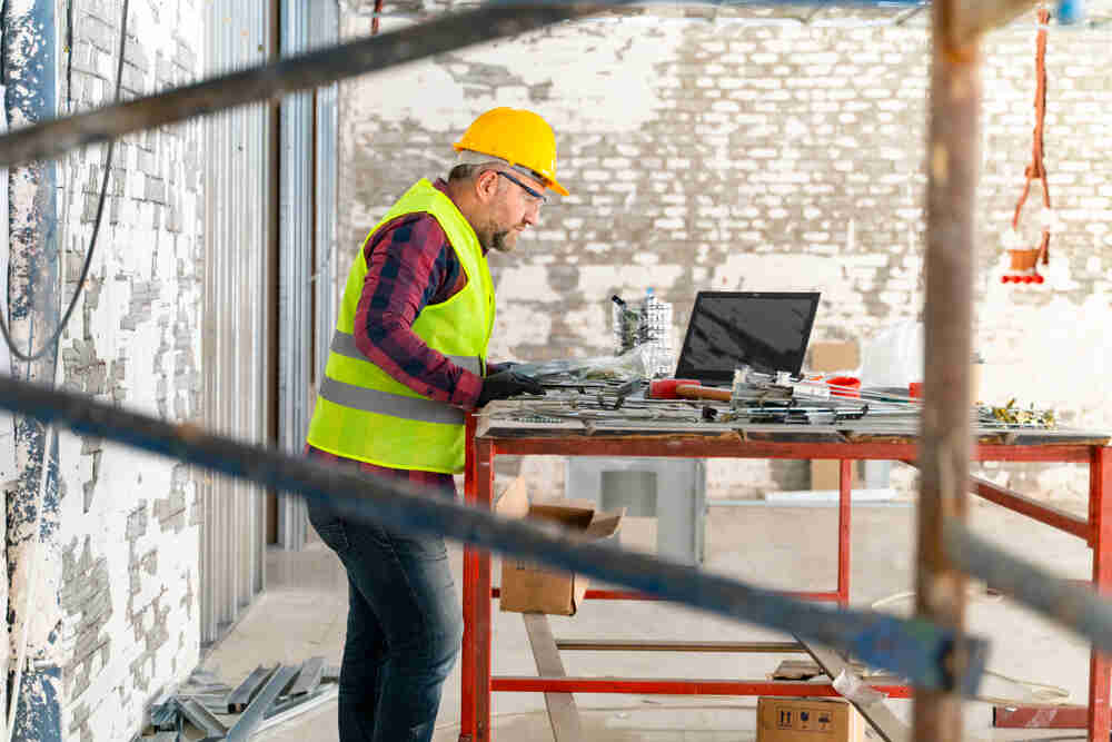 A construction worker works on laptop at a construction site