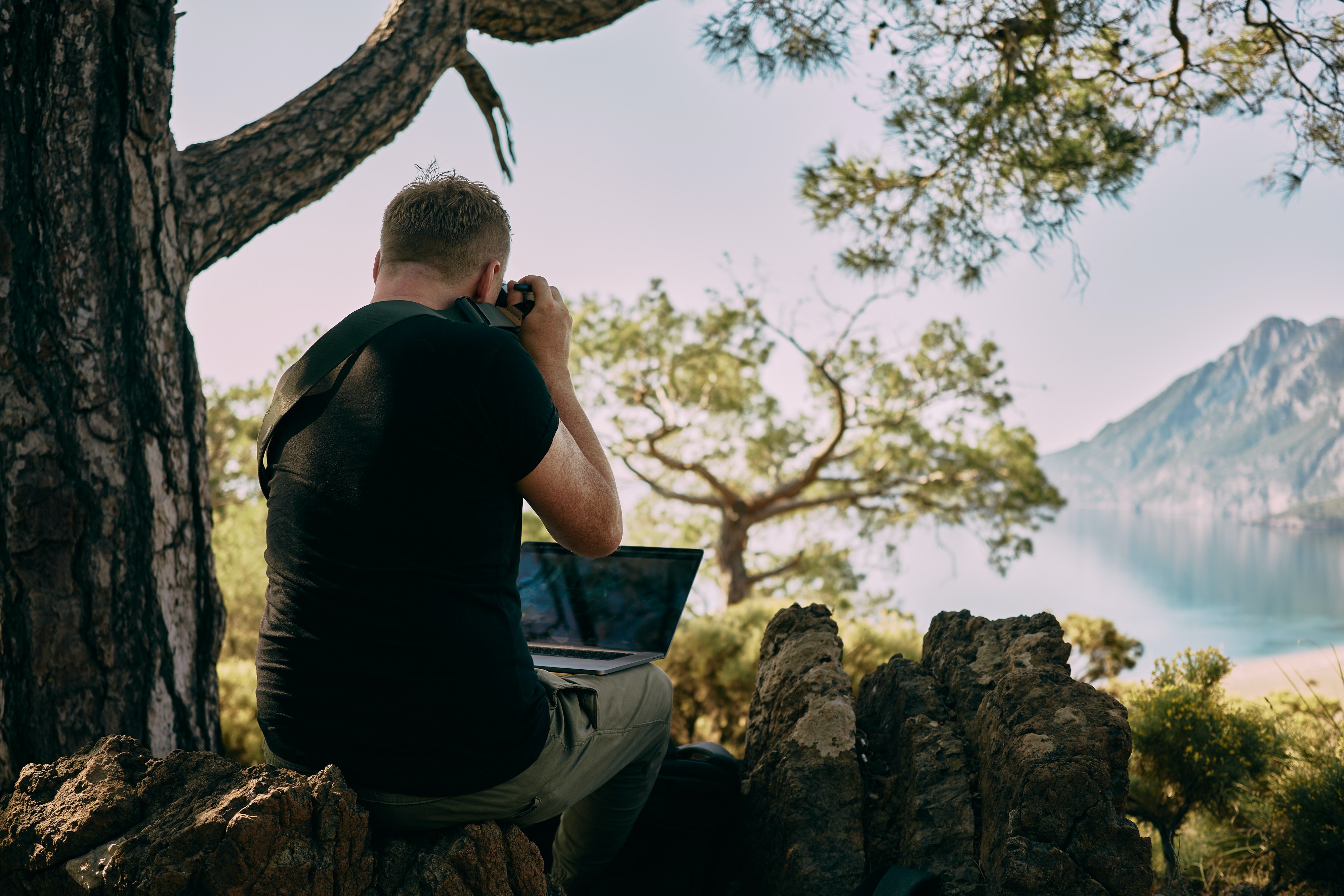 Man sitting on rock taking a picture, laptop on lap