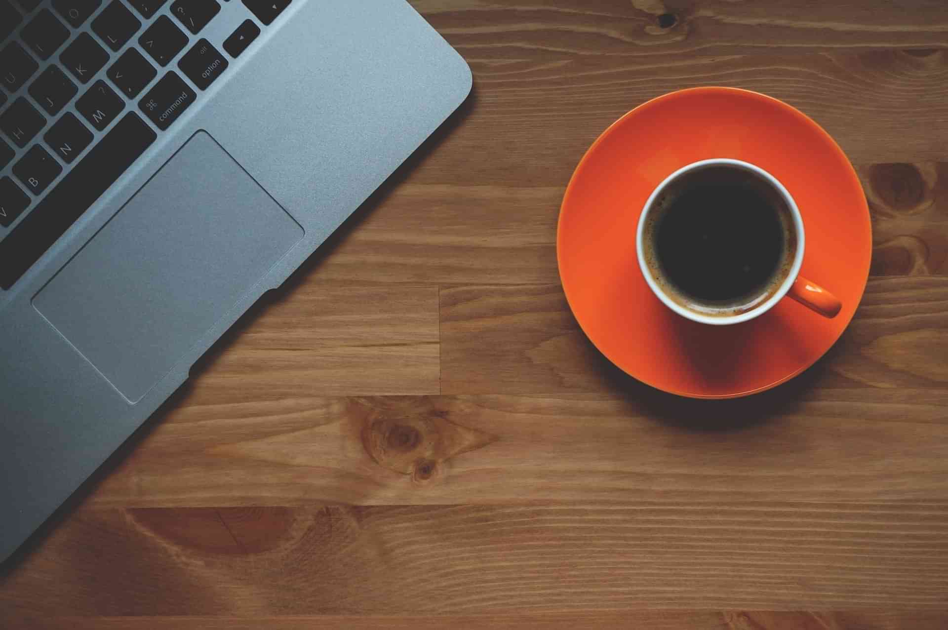 Laptop computer on a table next to a cup of coffee on a saucer