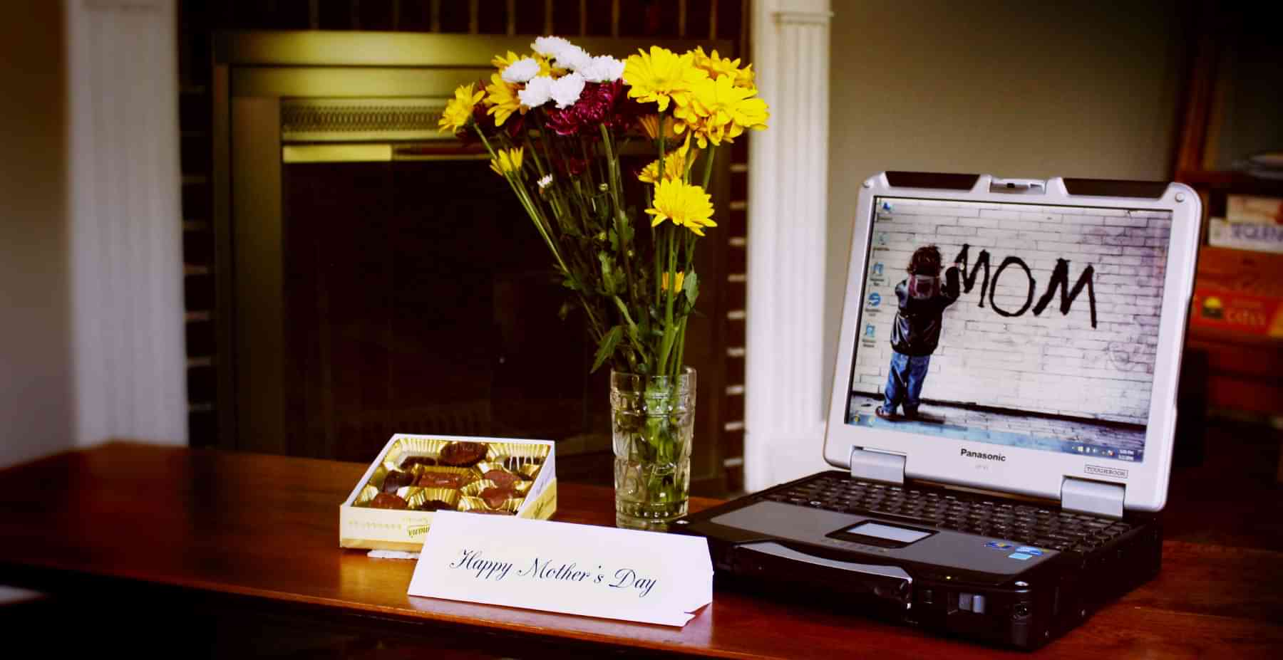Laptop on table with flowers in a vase and a box of chocolates